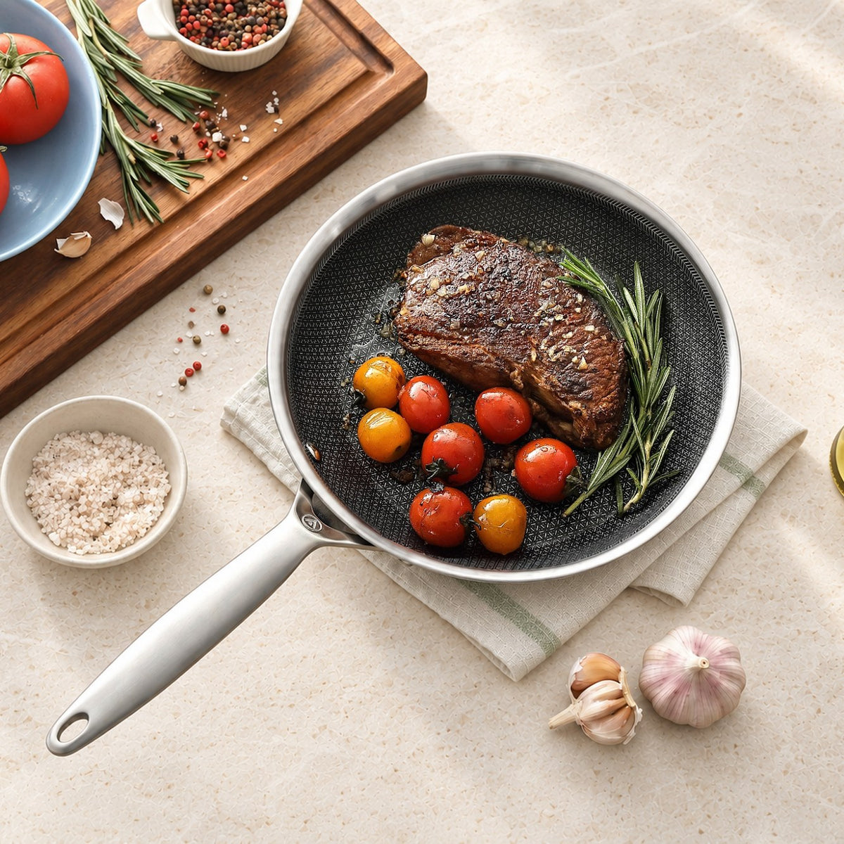 Bøf med cherrytomater og rosmarin i stegepande i 3-Ply Hybrid på lys sten, set ovenfra