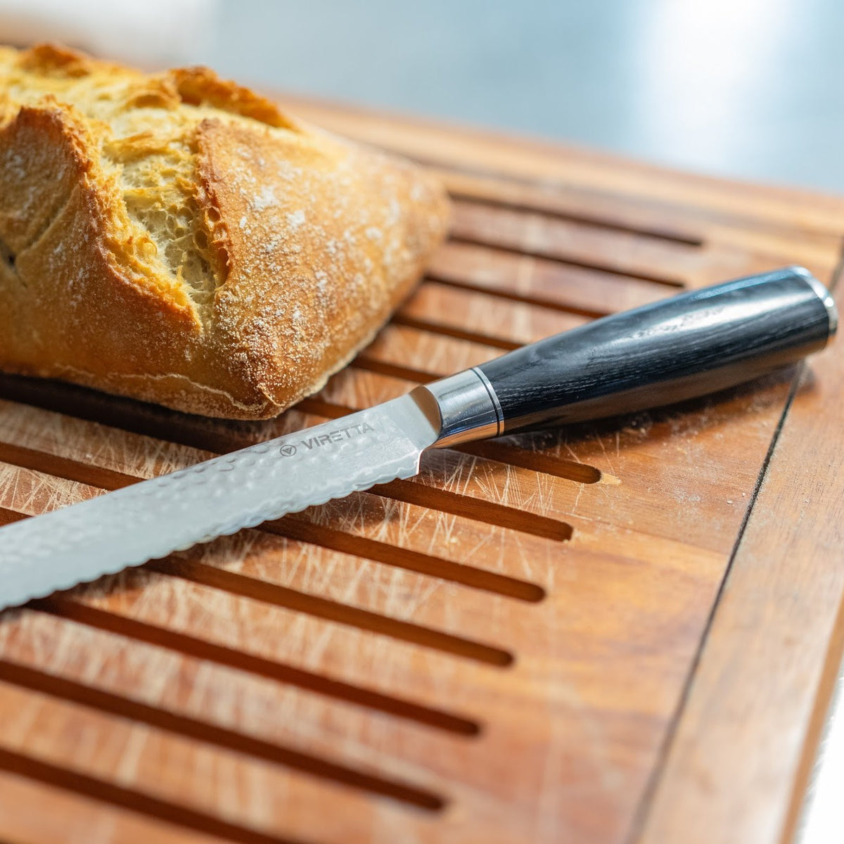 Shōjin Taru brødkniv med hamret klinge ved et surdejsbrød på et brødbræt