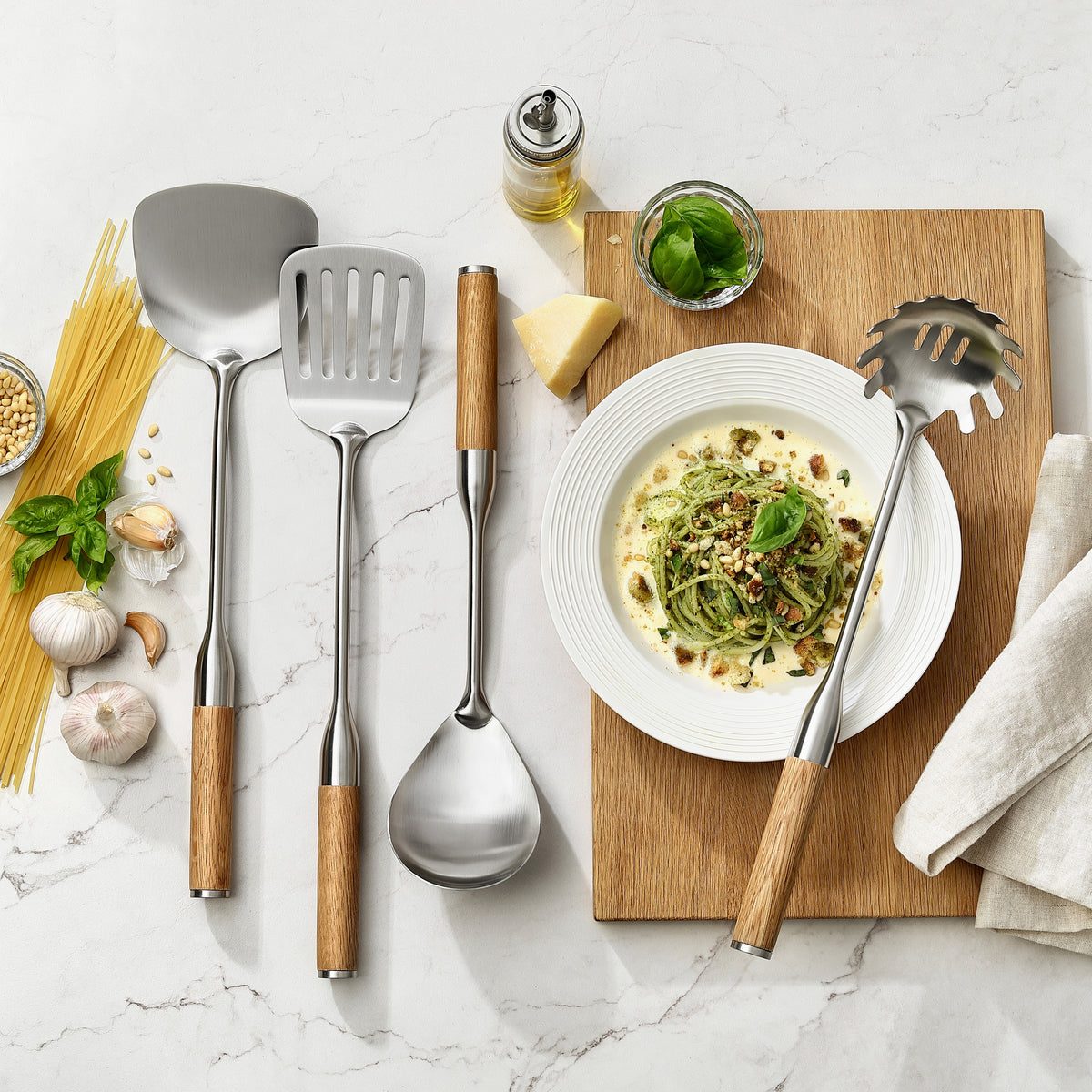 Palet med huller, palet, pastaske og serveringsske med greb i eg ved en tallerken pasta med pesto