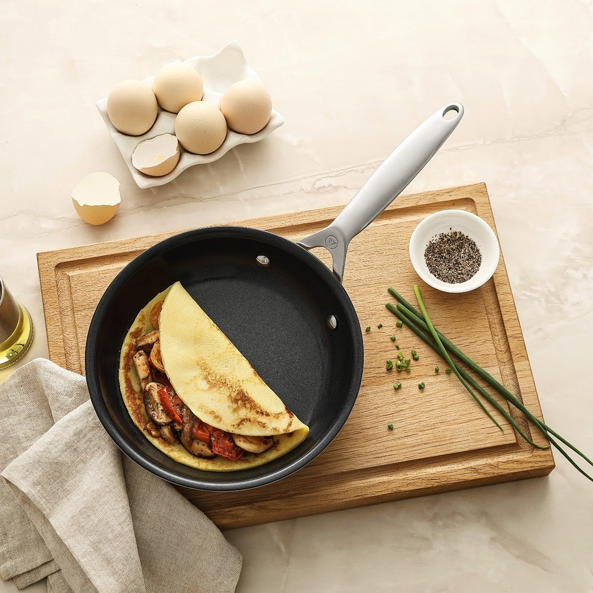 Foldet omelet med grøntsager i stegepande i 3-Ply keramisk på skærebræt