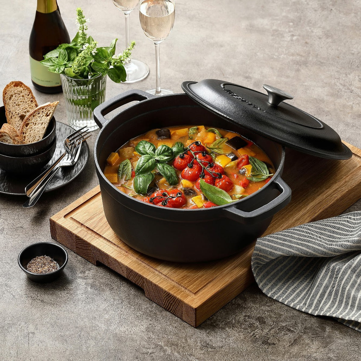 Skifersort støbejernsgryde med ratatouille og låget på skrå, på skærebræt
