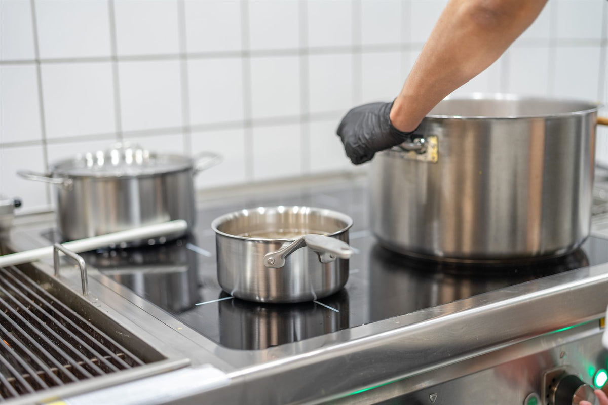 Gryder og en kasserolle i rustfrit stål på induktion i et restaurantkøkken