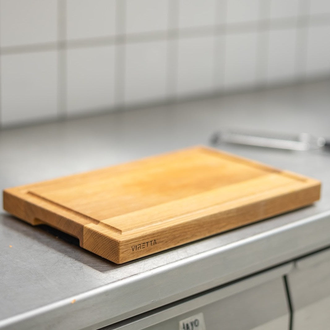 Skærebræt i eg med saftrille på et stålbord i et restaurantkøkken