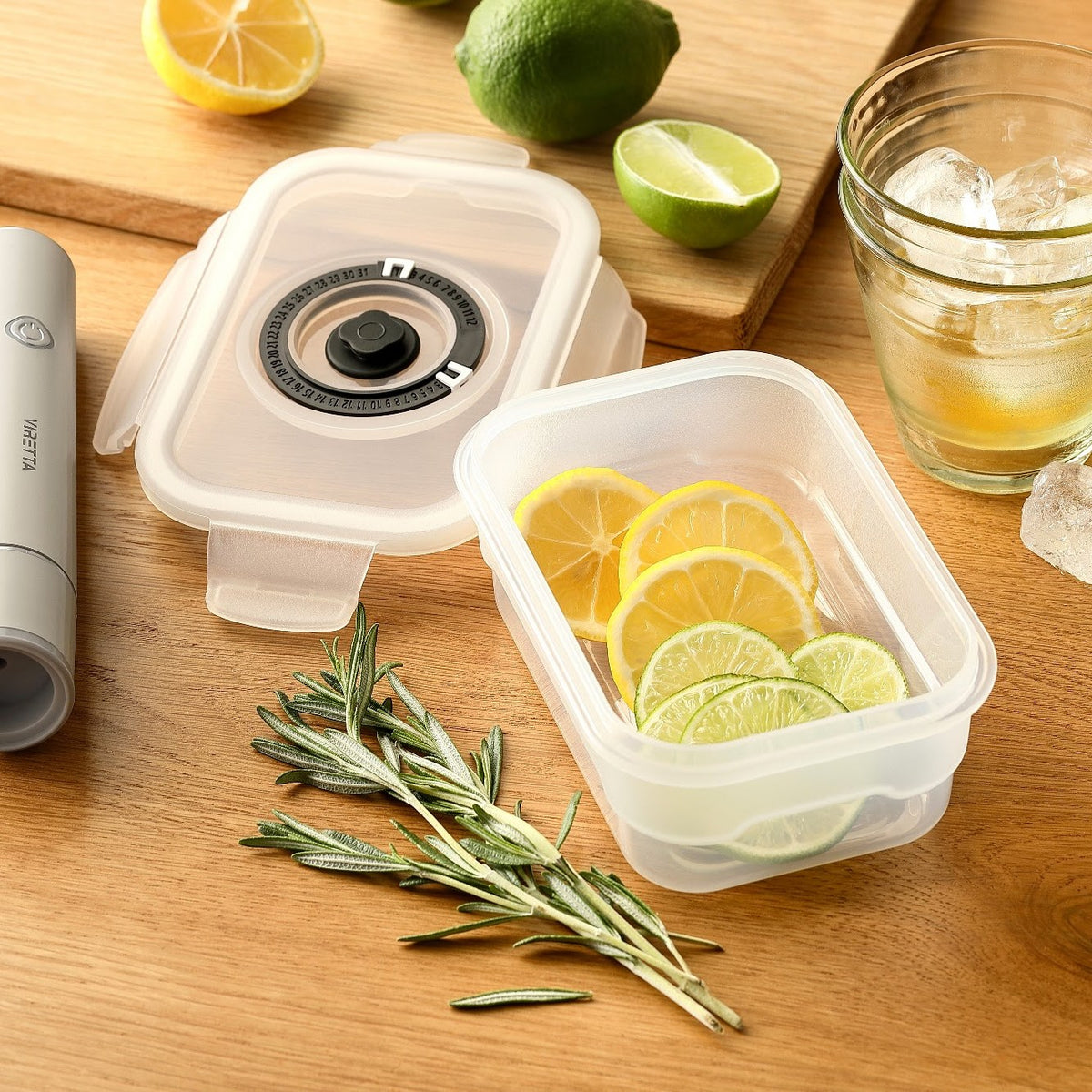 Vakuumbeholder i plast med citron- og limeskiver – låget og den elektriske vakuumpumpe ligger ved siden af