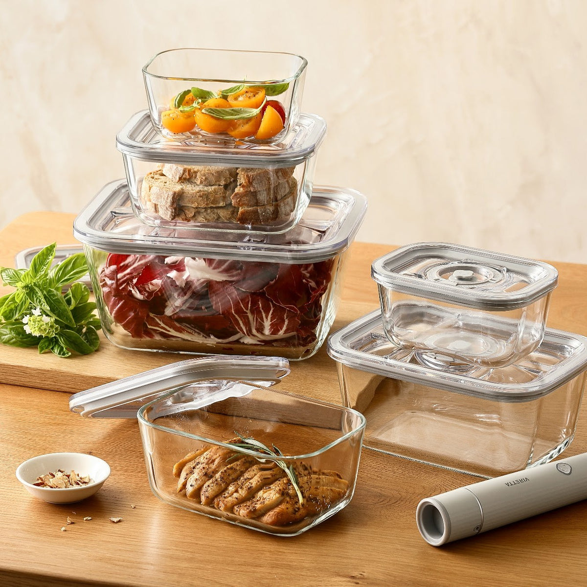 Vakuumbeholdere i glas med tomater, brød, salat og kylling på et spisebord