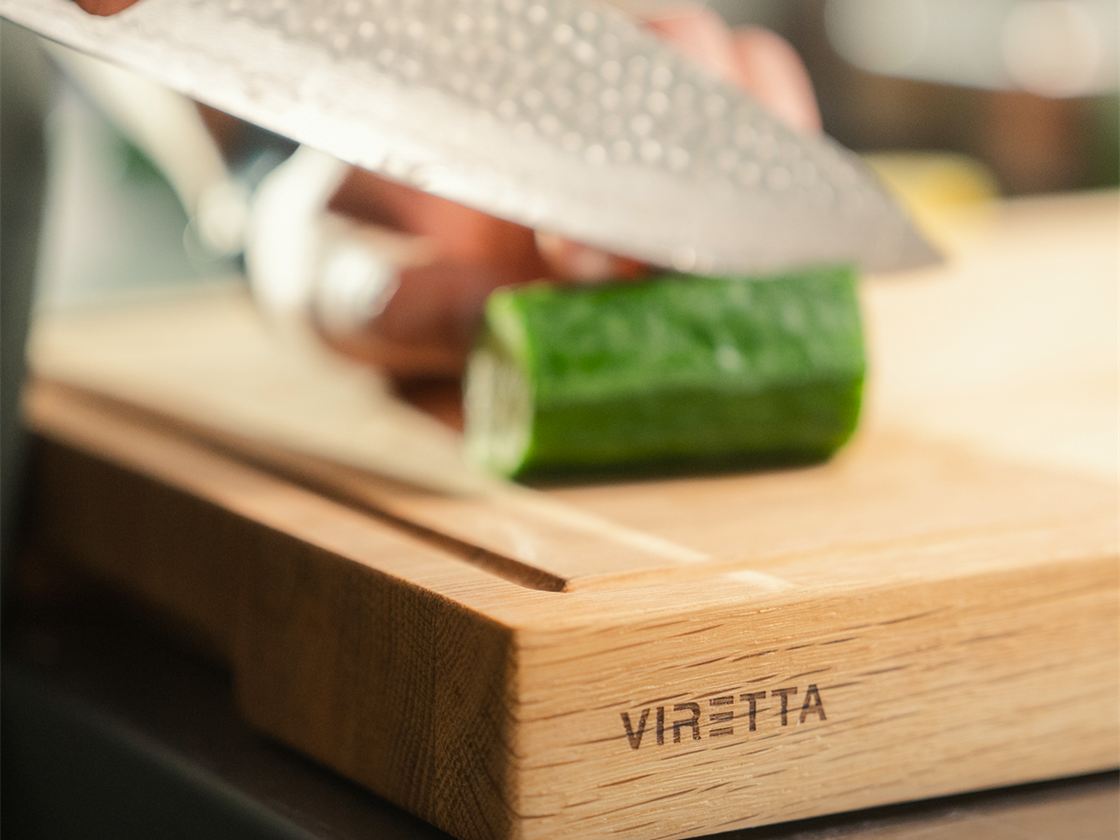 En kniv skærer agurk på et skærebræt i træ. Brættet har Viretta-logo